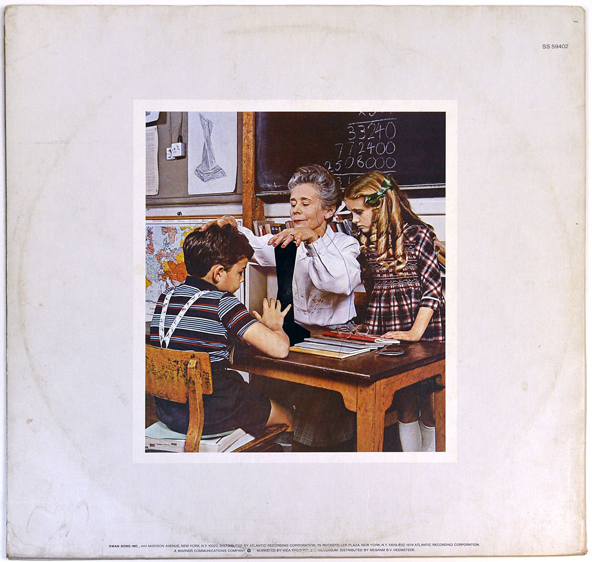 Back cover of Led Zeppelin's 'Presence' album, depicting a vintage classroom scene where a teacher gestures toward a mysterious black object on a desk, with two children looking on. A chalkboard with math problems and a sketch of the same black object are in the background.